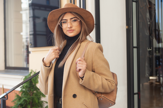 Jeune femme stylée en tenue automnale avec un manteau camel, des lunettes et un chapeau tendance, incarnant l'essence de notre guide sur la manière d'accessoiriser votre tenue avec des pièces Milanoza pour une touche d'élégance personnelle.