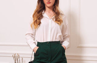 Femme élégante en chemisier blanc et pantalon vert, style professionnel décontracté.