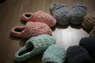 Assortiment de chaussons douillets en sherpa dans une variété de couleurs pastel sur un sol en bois.