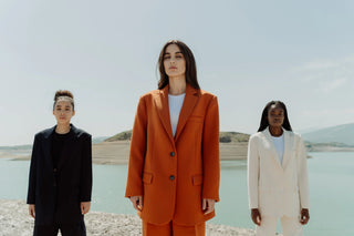 Trois femmes dégageant confiance et style en costumes élégants, des nuances monochromes de blanc, orange et noir, reflétant la diversité et la force féminine.