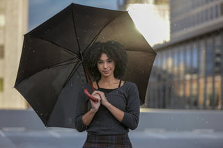 Femme élégante tenant un parapluie noir sous une pluie légère, incarnant la protection avec style en milieu urbain.