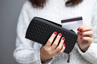 Main féminine élégante tenant un portefeuille tressé noir avec des ongles vernis en rouge, illustrant le style et la fonctionnalité.