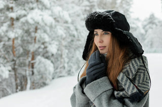 Femme portant des gants élégants et un chapeau d'hiver tout en regardant par-dessus son épaule dans un paysage enneigé.