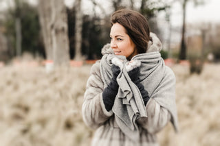 Femme enveloppée dans une écharpe grise douillette, évoquant chaleur et confort en hiver.