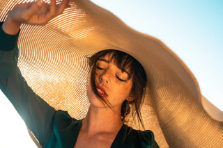 Jeune femme élégante portant un large chapeau de paille sous le soleil, évoquant le style et la protection solaire.