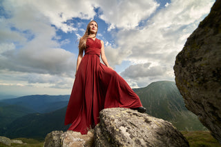 Élégante robe longue rouge drapée, portée par une femme majestueuse se tenant sur un rocher avec un paysage montagneux en arrière-plan.