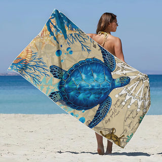 Femme portant une grande serviette de plage bleue avec motif de tortue marine utilisée comme châle sur une plage ensoleillée - Milanoza
